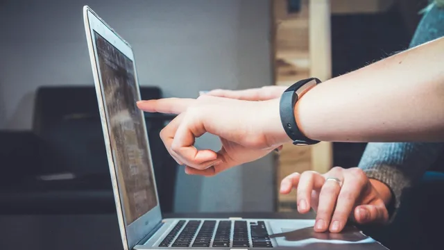 A person's hands at a laptop with the screen lit.
