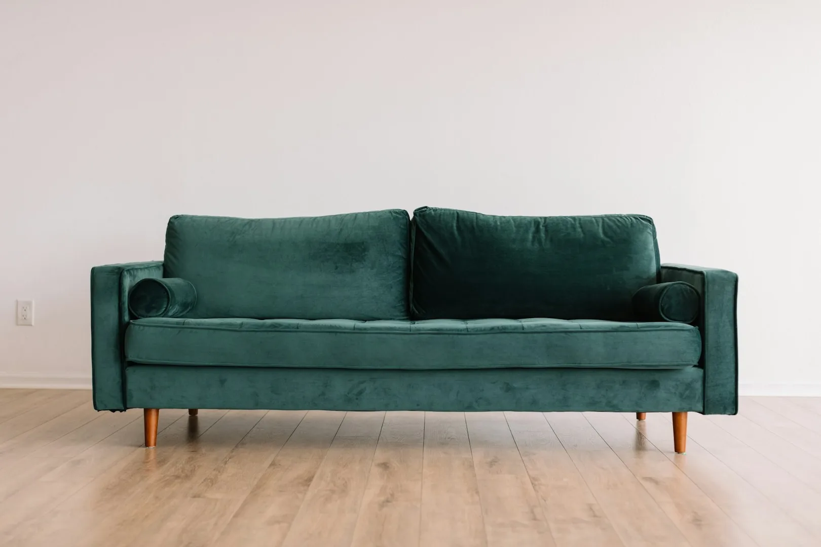 A green velvet sofa against a pale wall.