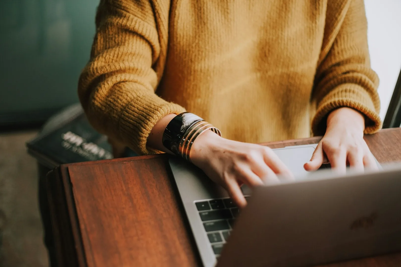A person sitting at a wooden desk in front of a laptop.